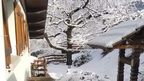 A stone pathway leading to a wooden bench under a covered area, with snow-covered trees and a clear sky in the background.