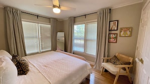 Une chambre à coucher comprenant un lit, une chaise, un ventilateur de plafond et une fenêtre avec des stores.