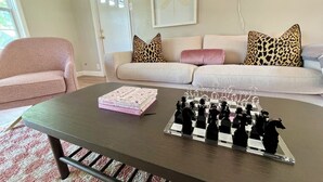 Un salon avec un jeu d’échecs posé sur une table basse, un canapé orné de coussins à motifs léopard et un panneau néon sur lequel on peut lire « The Dreamhouse ».
