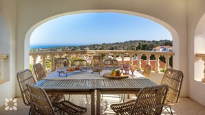 A terrace with a table set for two, overlooking a scenic view of the sea and hills. - Villa PERLA by Abahana Villas (Teulada)