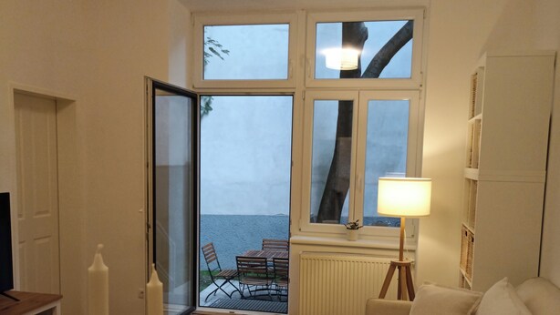 Una sala de estar con una mesa de madera, un sofá blanco, una lámpara y vistas amplias por un gran ventanal.