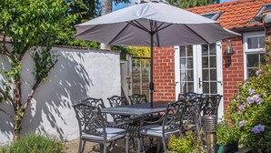 Een terras met een tafel, stoelen, een grote parasol en een stenen huis op de achtergrond.