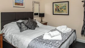 Een net opgemaakt bed met beddengoed met een patroon, een bedlampje en een lijst met een afbeelding van Scarborough.