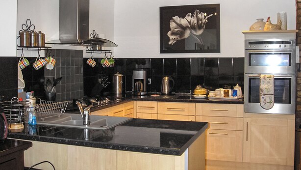 Een moderne keuken met een zwart aanrecht, roestvrijstalen apparatuur, houten kastjes en een hangende rek voor pannen.