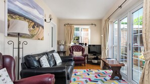 Een woonkamer met een zwarte leren bank, een rode fauteuil, een televisie en een kamerbreed tapijt met een patroon.