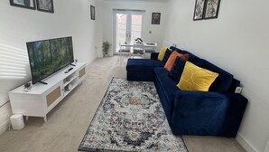 Un salon avec un téléviseur, un canapé bleu agrémenté de coussins colorés, un tapis à motifs et un meuble blanc.