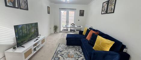 A living room with a TV, a blue sofa with colorful cushions, a patterned rug, and a white cabinet.
