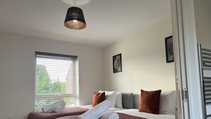 Une chambre d’hôtel avec deux lits, une grande fenêtre avec des stores, un luminaire suspendu et une porte avec une poignée.