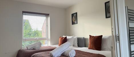 Habitación de hotel con dos camas, un ventanal con persianas, una lámpara colgante y una puerta con picaporte.