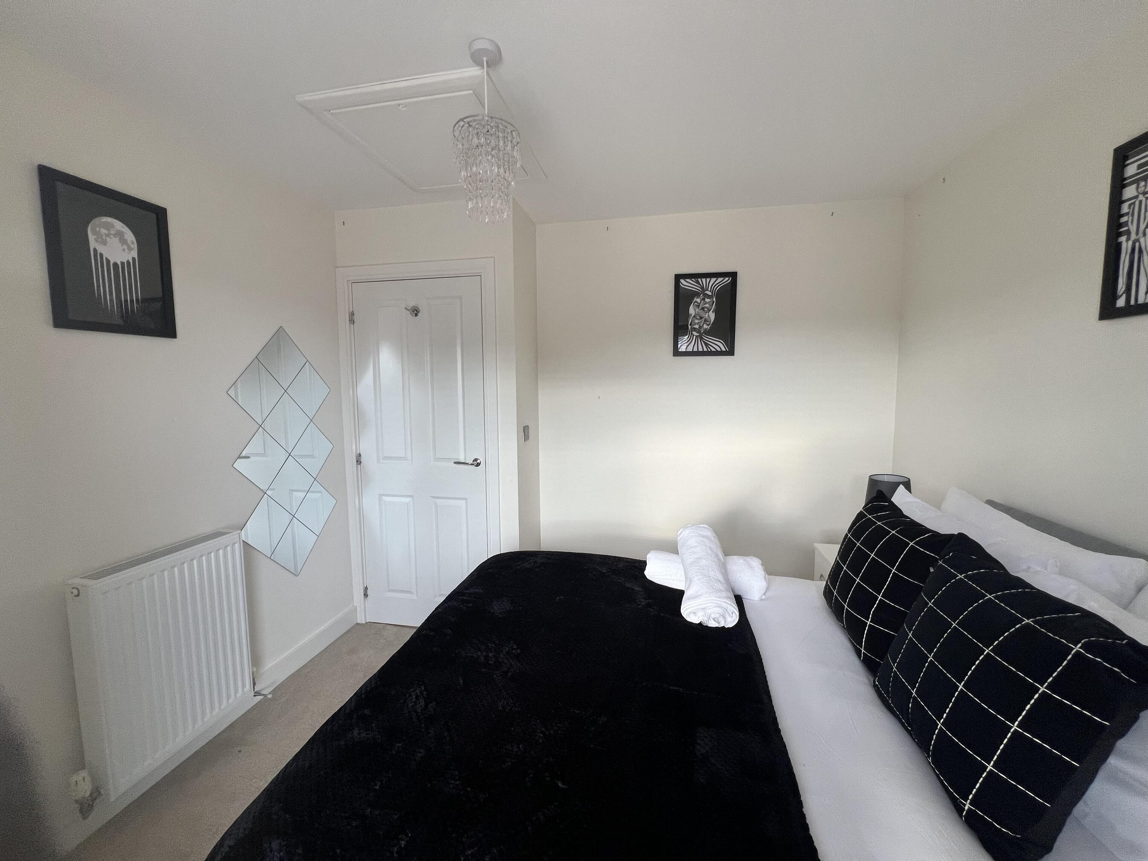 Een slaapkamer met een zwart beddeken, witte kussens en een witte deur.