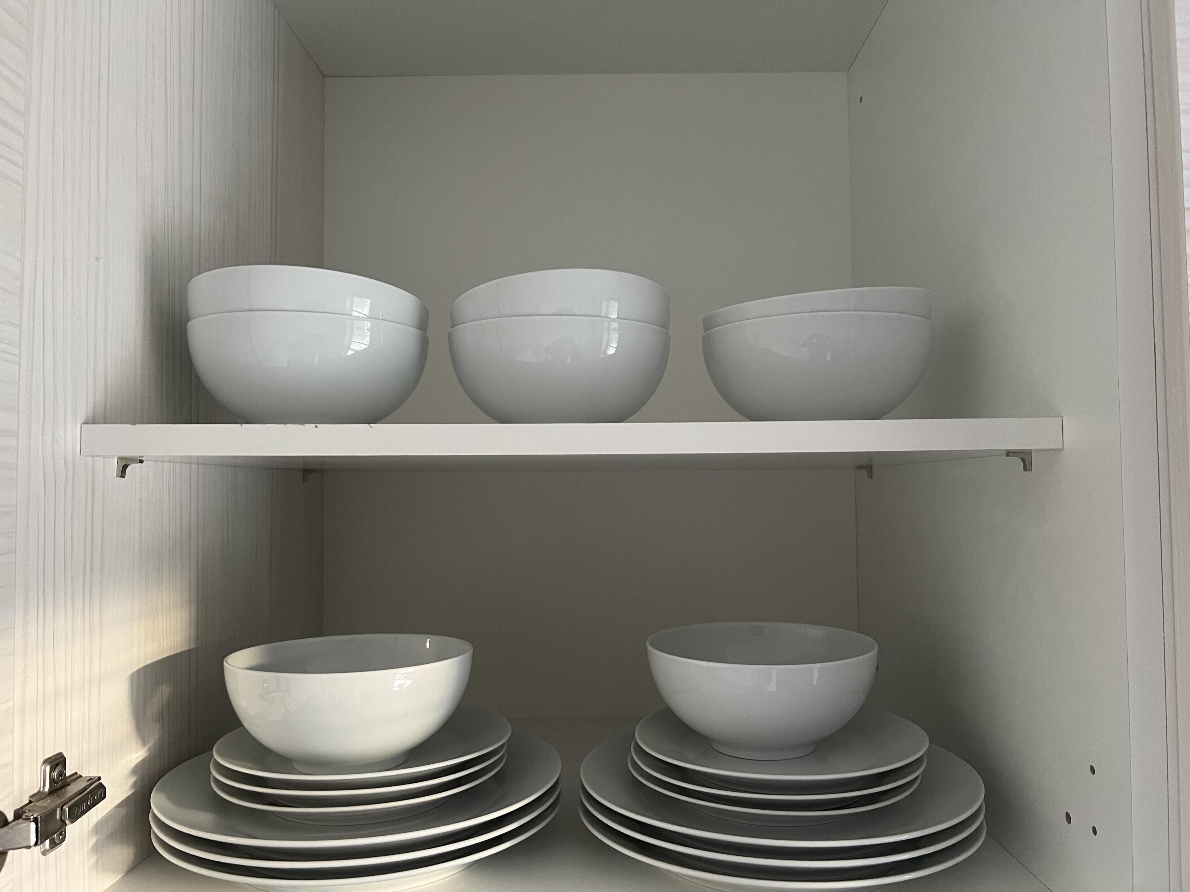 Una cocina con armarios blancos y un estante con cuencos y platos.