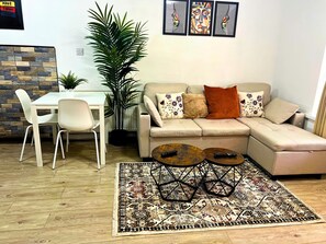 A living room with a sofa, two coffee tables, a dining table with chairs, and a large plant. - Apartment Sleeps 4 With Garden (Birmingham)