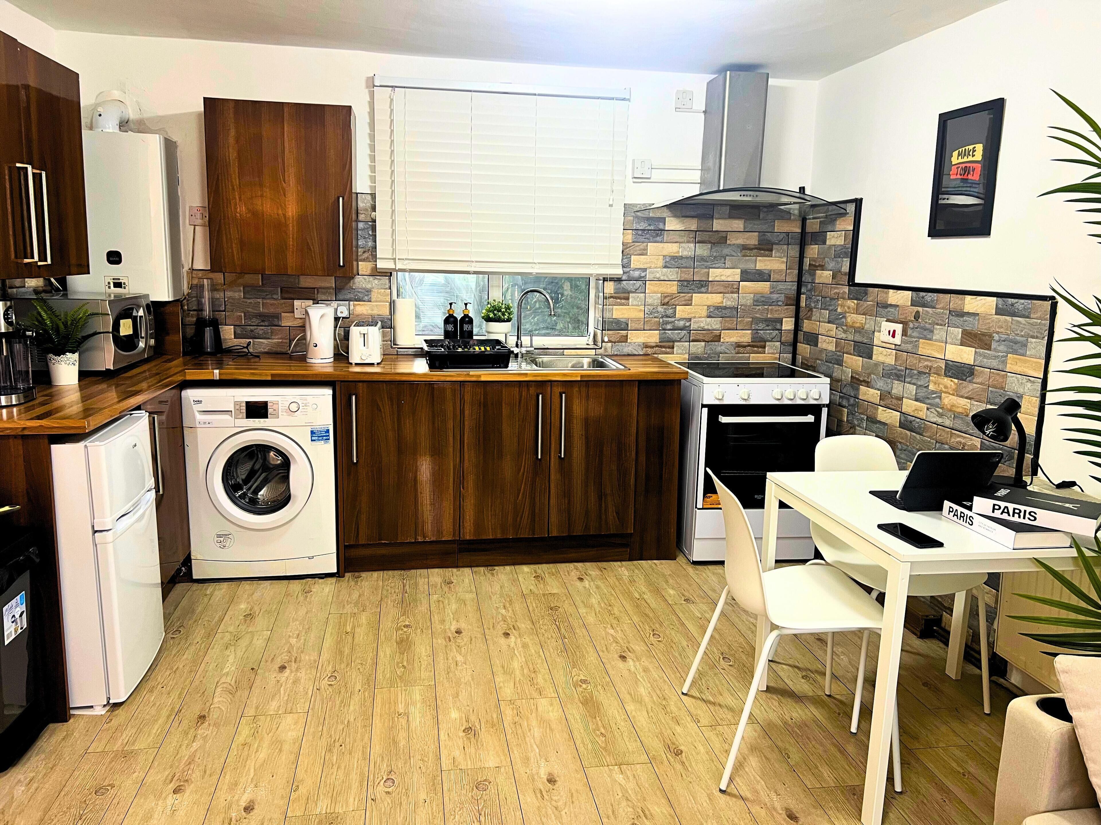 A compact kitchen with wooden cabinets, a built-in oven, a washing machine, and a dining area with a table and chairs.