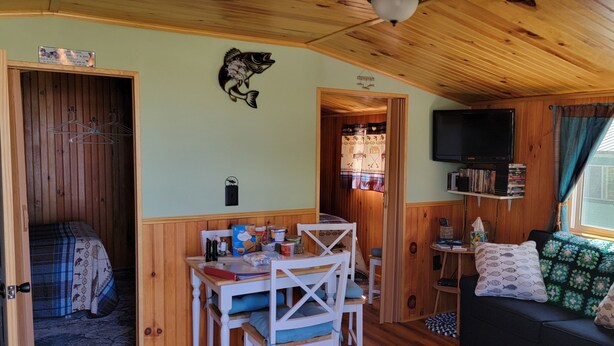 Interior acolhedor de uma cabana com área de jantar, sofá, TV e teto de madeira.