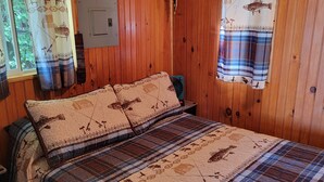 Um quarto acolhedor com paredes de madeira, uma cama com roupa de cama estampada e cortinas com desenhos de peixes.