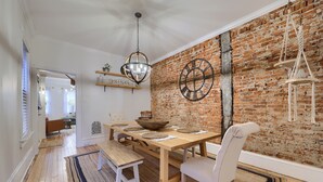 A dining area with a brick wall, wooden table, white chairs, and a hanging light fixture. - Cityside on North Prince, in Historic Downtown Lancaster (Lancaster)