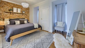 A bedroom with a brick wall, a bed, a chandelier, a mirror, and a chair. - Cityside on North Prince, in Historic Downtown Lancaster (Lancaster)