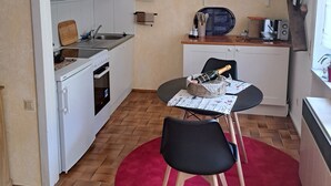 Een kleine keuken met witte kasten, een eettafel met stoelen, een rode vloerkleed en een hangende hanglamp.