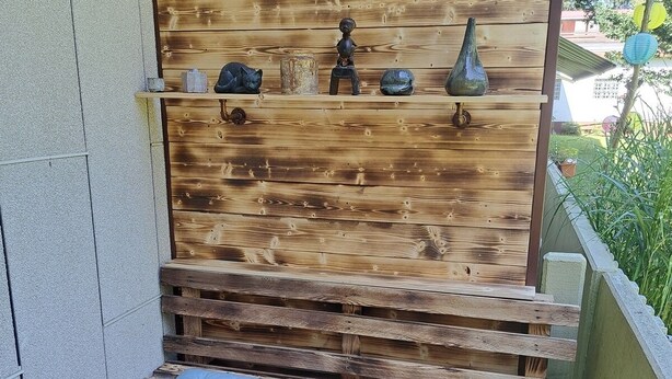 Een houten bank met kussens, een tafeltje en decoratieve objecten aan een muur.