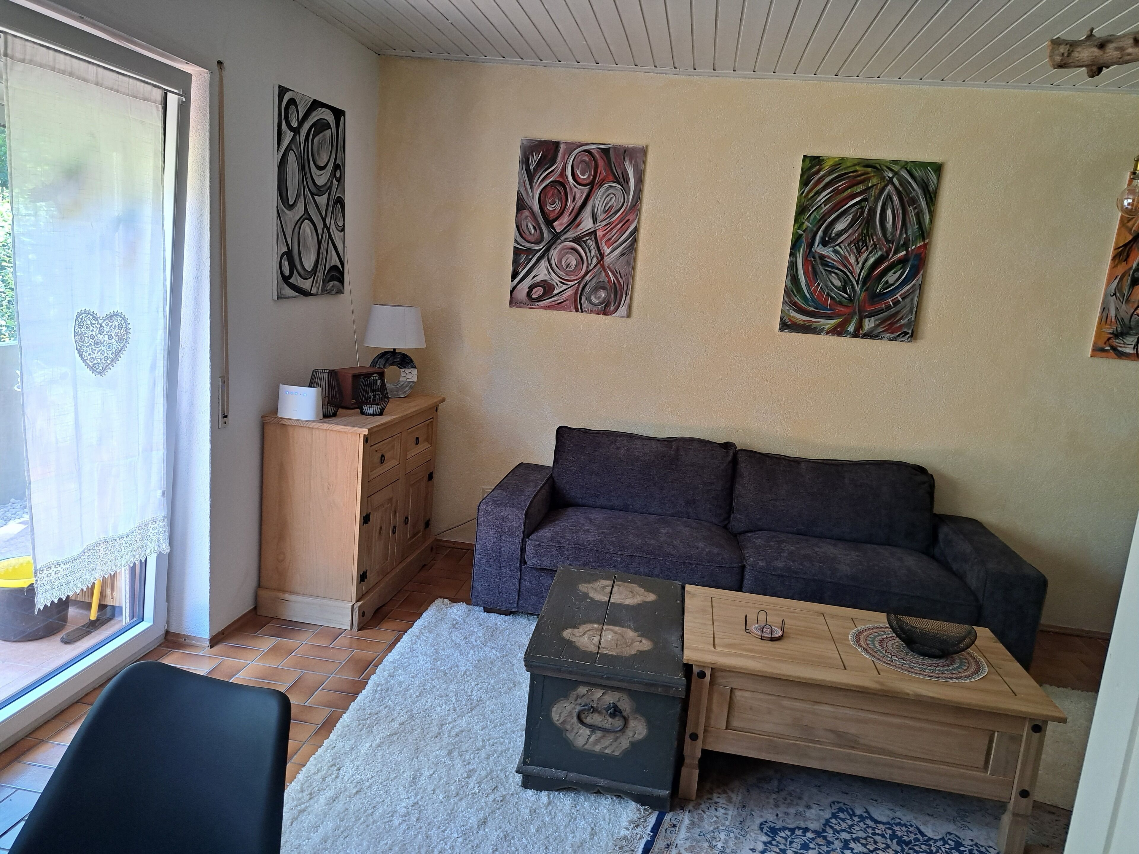 Una sala de estar con un sofá, un aparador de madera, una mesita y pinturas abstractas en la pared.