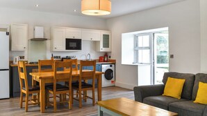 A compact kitchen with white cabinets, a microwave, a washing machine, and a dining area with wooden chairs and a table. - 3 bedroom accommodation in Llanilar, near Aberystwyth (Llanilar, near Aberystwyth)