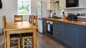 A modern kitchen with a wooden dining table, cabinets, a stove, and a microwave. - 3 bedroom accommodation in Llanilar, near Aberystwyth (Llanilar, near Aberystwyth)