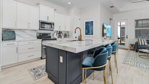 A modern kitchen with white cabinets, a large island with bar stools, a microwave, and a sink. - New 2 Bedroom + Den, 2 Bath Home w/2 Car Garage 10 Min from Downtown Naples (Naples)