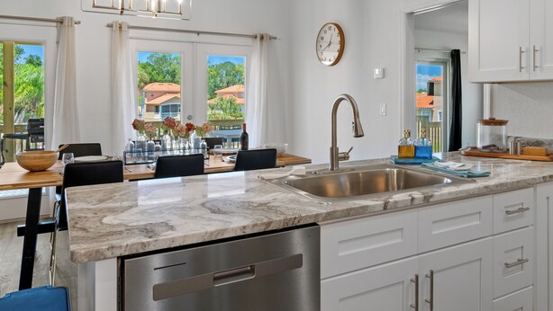 A modern kitchen with a marble countertop, stainless steel appliances, and a dining area with a view of the outdoors. - New, August 2024! Beautiful porch, view of Marina (Homosassa)
