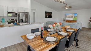 A modern kitchen with stainless steel appliances, a dining area with a wooden table set for four, and a living area with a sofa and a TV. - New, August 2024! Beautiful porch, view of Marina (Homosassa)