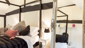 Een slaapkamer met een hemelbed, een spiegel, een nachtkastje en een open haard.