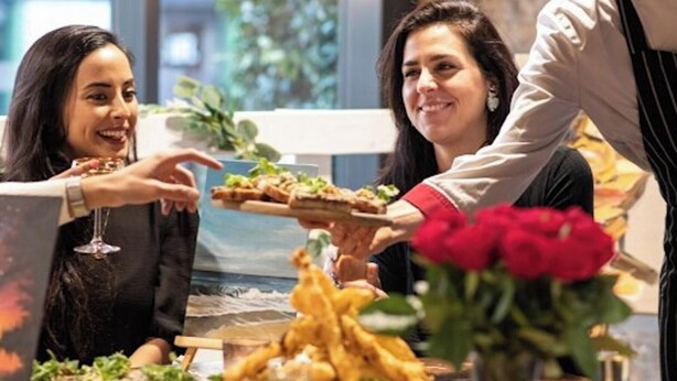 Een eettafel met eten, een glas wijn en een ober in dienst.