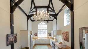 Een ruime keuken met een groot raam, een kroonluchter en een rustiek houten plafond.