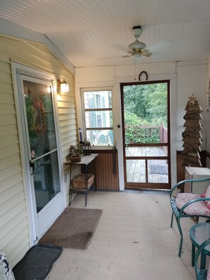 A covered porch with a sliding glass door, a small table, chairs, a ceiling fan, and a view of the backyard. - Charming 2-bedroom cottage near Bedford, screened porch deck & private setting (Bedford)