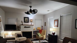 Un salon avec une cheminée, un téléviseur et un ventilateur de plafond.