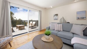A modern living room with a grey sofa, a round coffee table with a plant, and a balcony with outdoor furniture. - Entire Oceanview Coastal Retreat in Pacifica (Pacifica)