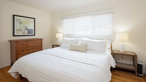 A bedroom with a large bed, two bedside tables with lamps, a wooden dresser, and a framed picture on the wall. - Entire Oceanview Coastal Retreat in Pacifica (Pacifica)