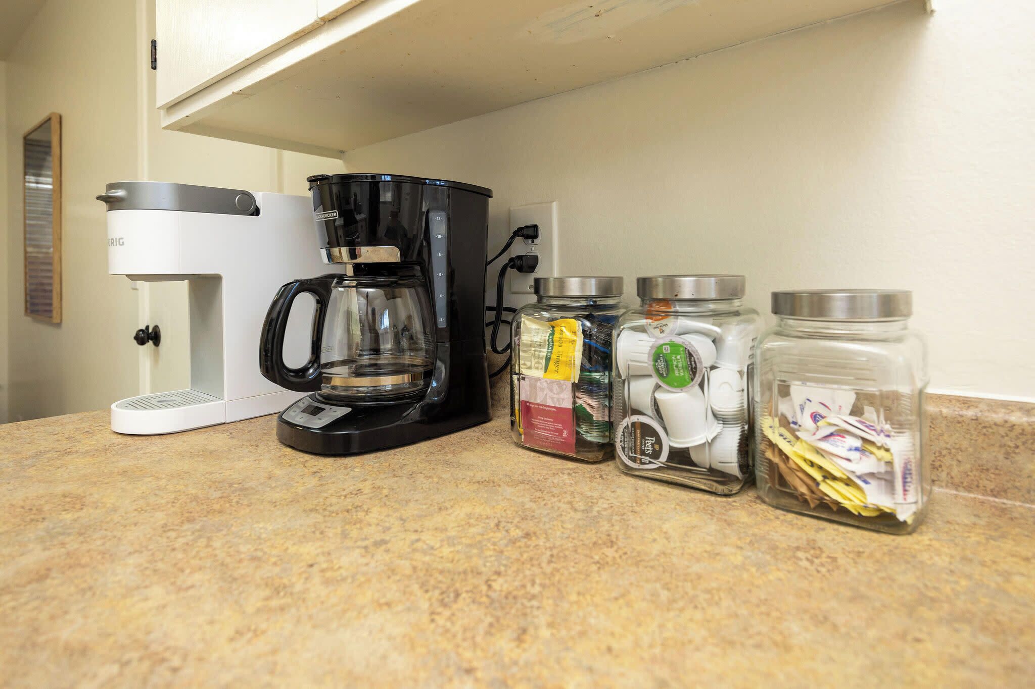 A kitchen counter with a coffee maker, a blender, and three glass jars with lids.