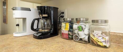 A kitchen counter with a coffee maker, a blender, and three glass jars with lids.