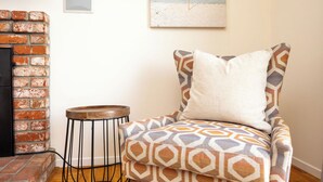 A cozy room with a brick fireplace, a patterned armchair, and a small round table. - Entire Oceanview Coastal Retreat in Pacifica (Pacifica)
