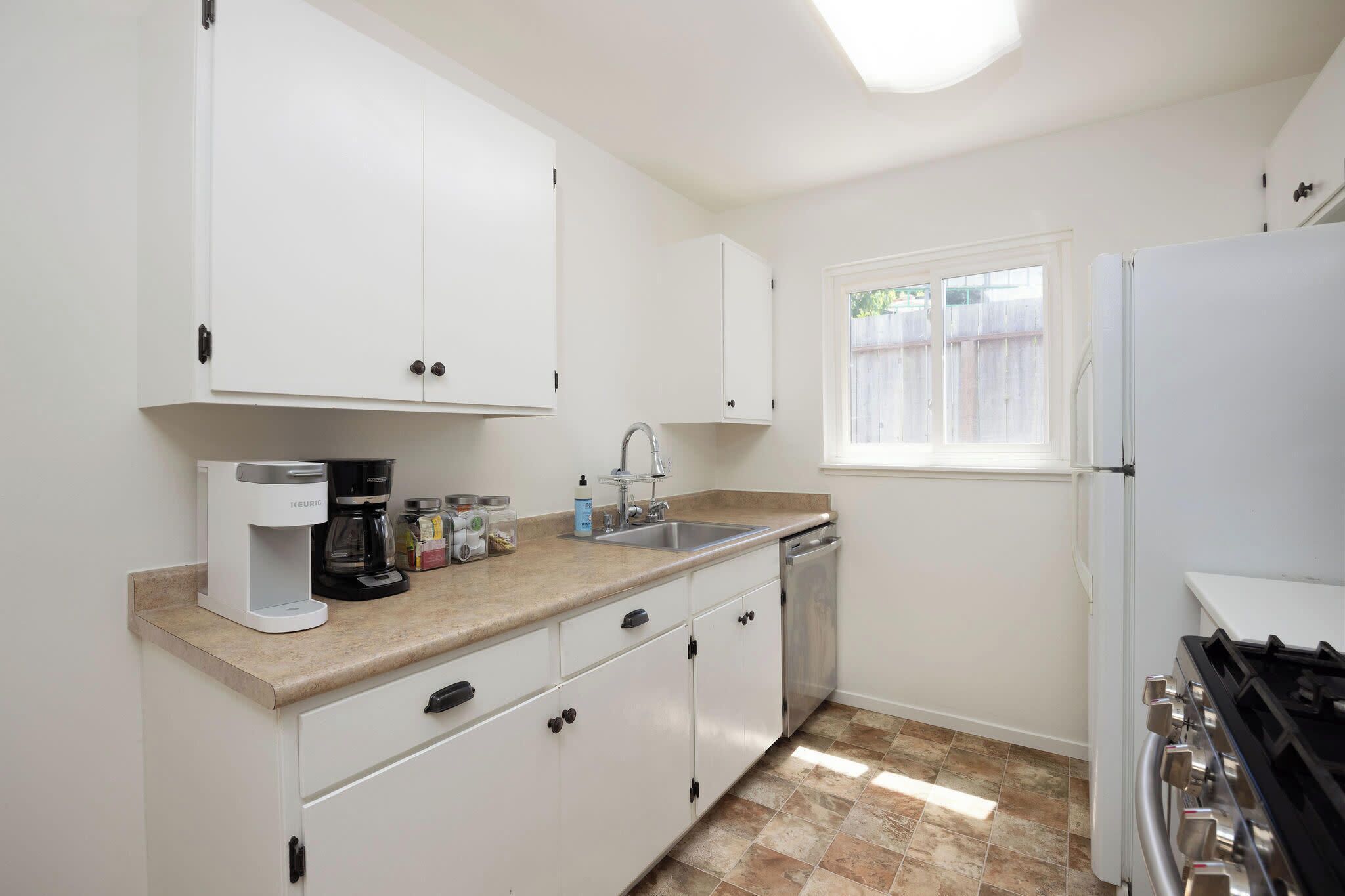 A kitchen with white cabinets, a coffee maker, a sink, and a stove.