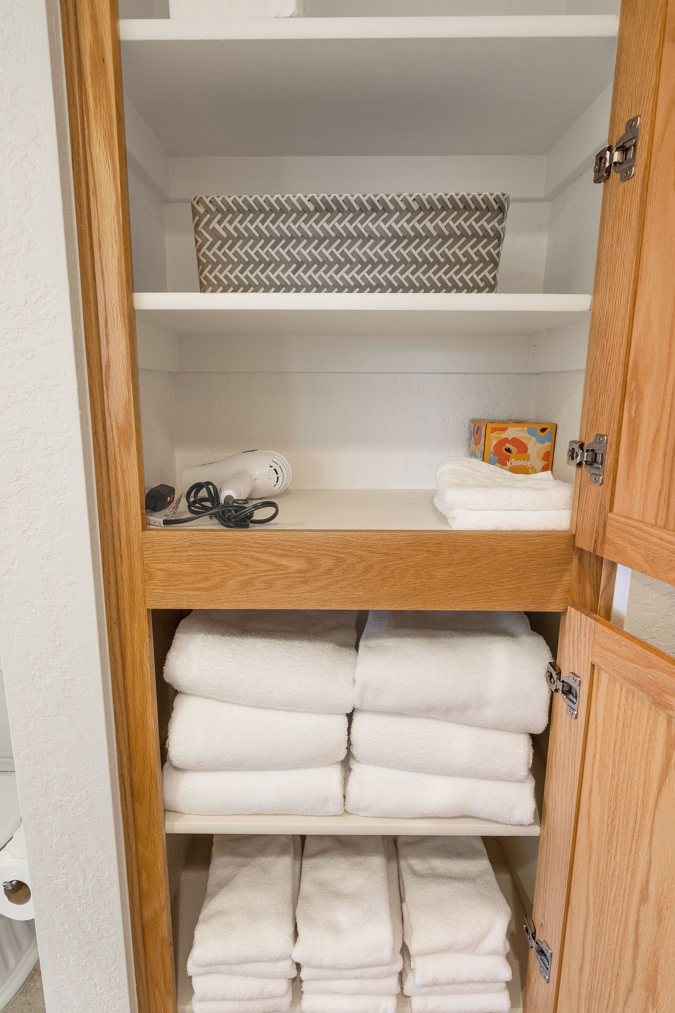 A wooden cabinet with multiple shelves, some holding folded towels and a hairdryer.