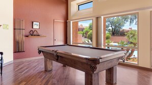 A pool table in a room with large windows, wooden floors, and a view of a swimming pool and greenery outside. - Charming one bedroom in a gated community near Sabino Canyon with heated pool. (Tucson)
