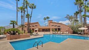 A swimming pool with lounge chairs and palm trees, surrounded by a building with a desert landscape in the background. - Charming one bedroom in a gated community near Sabino Canyon with heated pool. (Tucson)