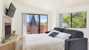 A modern bedroom with a bed, a TV mounted on the wall, a fireplace, and a balcony with a view of the city. - Charming one bedroom in a gated community near Sabino Canyon with heated pool. (Tucson)
