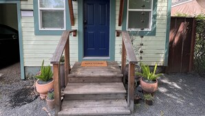 Une maison avec une porte bleue, un porche en bois et des plantes en pot.