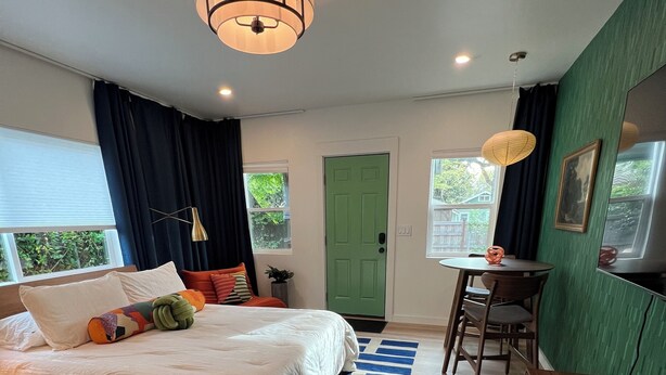 Une chambre à coucher avec un lit, un bureau, une chaise, une porte verte et une fenêtre.