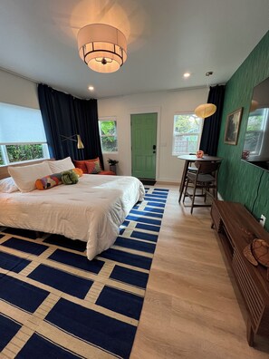 Un dormitorio con cama, escritorio, silla, una puerta verde y una ventana.
