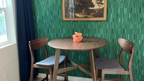 Un coin repas comprenant deux chaises en bois, une table ronde, un tableau encadré et un luminaire suspendu.
