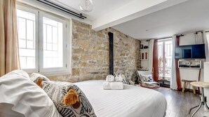 A bedroom with a large bed, a stone wall, a TV, and a small table.