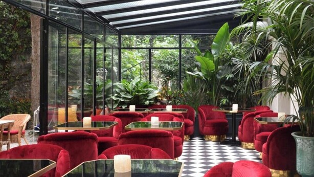 A conservatory with red chairs and tables, surrounded by lush greenery.